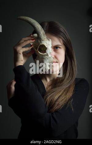 Portrait d'une jeune fille brune se tenant la moitié d'un crâne de chèvre devant son visage, duplicité concept Banque D'Images