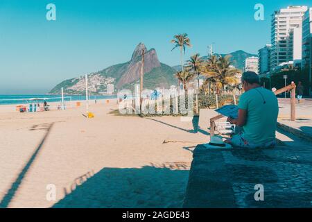 RIO DE JANEIRO, Brésil - le 14 mai 2019 : la lecture de l'actualité dans la plage d'Ipanema, avec le magnifique paysage. Banque D'Images