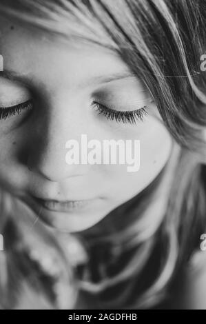 Photo verticale en niveaux de gris d'une petite fille mignonne avec fermé les yeux qui font un souhait Banque D'Images