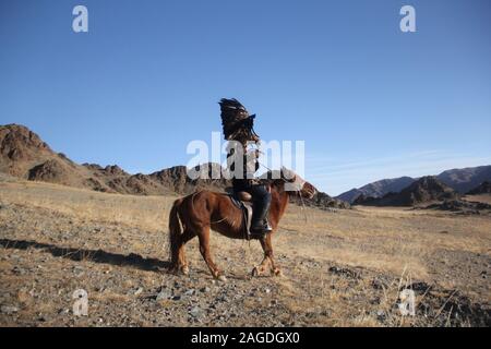 Image d'un cavalier avec un aigle noir sur un cheval brun entouré de rochers sous un ciel bleu Banque D'Images