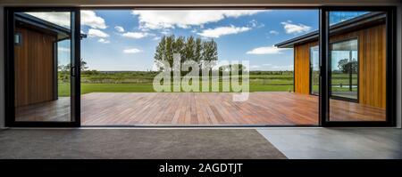 Vue depuis une maison moderne avec de grandes portes vitrées dans le champ vert Banque D'Images