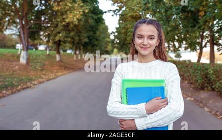 Happy girl smiling adolescent joyeux joyeux, se trouve parc d'été les arbres d'automne, l'arrière-plan de l'espace libre pour copier du texte. Dans les manuels de l'ordinateur portable mains note Banque D'Images