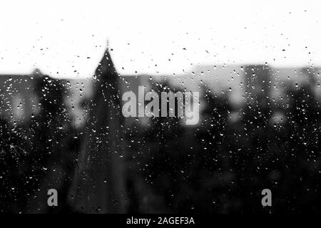 Prise de vue en niveaux de gris d'un verre recouvert de gouttes de pluie avec un arrière-plan flou Banque D'Images