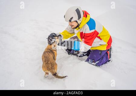 Young male snowboarder joue avec les chiots dans une station de ski en hiver Banque D'Images