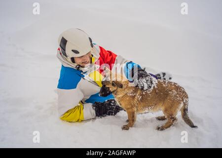 Young male snowboarder joue avec les chiots dans une station de ski en hiver Banque D'Images