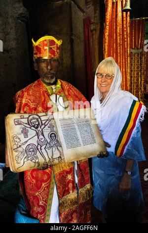 L'Éthiopie, région d'Amhara, Arbatu Ensessa, Lalibela, Biblia Chirkos, prêtre en robe montrant 800 ans évangile éclairé avec crucifixion image pour s Banque D'Images