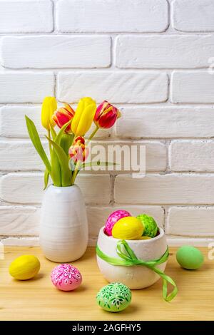 Arrangement de pâques avec rose, vert, jaune des oeufs décorés à la main, rouge et jaune tulipes au vase blanc Banque D'Images