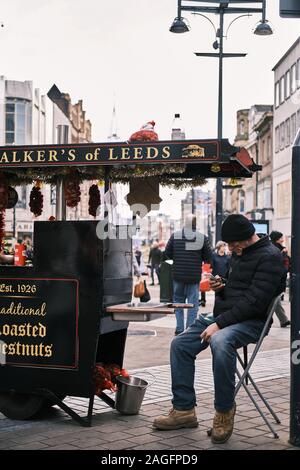 LEEDS, Royaume-uni - Mai 07, 2019 : free standing les noix rôties propriétaire reposant sur sa chaise alors que sur son mobile comme clients potentiels à pied par. Banque D'Images