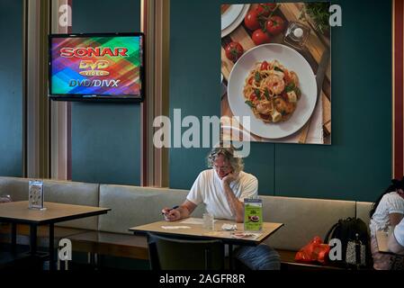 L'homme seul l'étude de documents dans un restaurant intérieur, contre un mur de toile de l'art de l'alimentation Banque D'Images