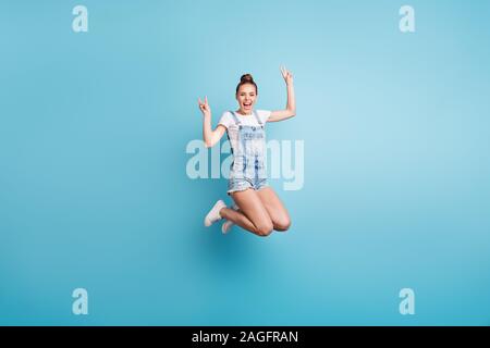 Toute la longueur de la taille du corps photo de heureux profiter de nice cute petite amie vous montrant v-sign lors d'un saut étant isolé avec fond bleu Banque D'Images