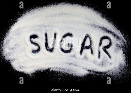 Sucre mot lettrage sur une main d'extraction de sucre blanc raffiné. Les cristaux de sucre de betterave granules sur un fond noir Banque D'Images