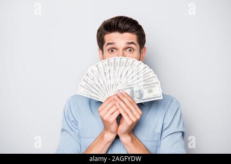 Photo de choqué funny funky joyeux guy cachant la moitié de son visage derrière l'argent qu'il a gagné de façon réussie de freelancing isolated over gray Banque D'Images