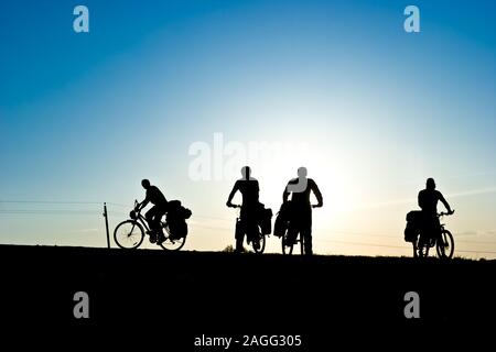 Groupe de cyclotouristes sur une route contre le coucher du soleil Banque D'Images