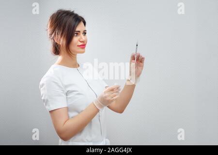 Jolie femme médecin aux cheveux noirs dans les gants de protection avec seringue debout contre un mur blanc, close-up Banque D'Images