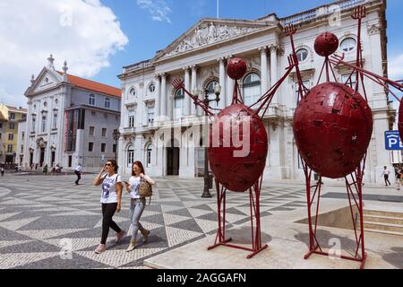 Lisbonne, Portugal : Deux jeunes femmes devant une statue de fer moderne à côté de l'Hôtel de ville néoclassique (Paços do Concelho) situé à la place de la ville (Praç Banque D'Images