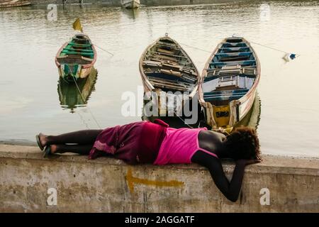 Saint Louis, Sénégal, Afrique de l'Ouest : Wolof girl resting par trois pirogues sur le fleuve Sénégal. Banque D'Images