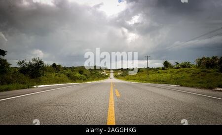 Routes rurales vide, Maranhao, Brésil. Une longue route droite vide et en milieu rural dans le nord du Brésil avec de gros nuages menaçants à l'horizon. Banque D'Images