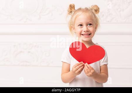 Petite fille adorable little red tient cœur fait de papper dans les mains. Banque D'Images