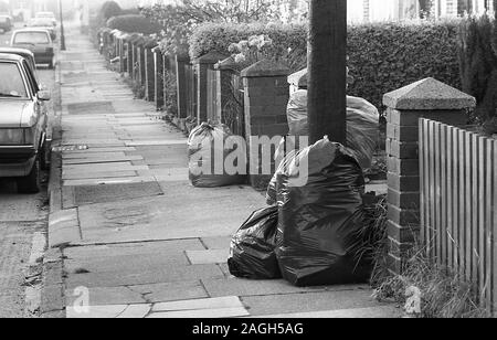 Années 1980, sacs historiques et poubelles se trouvant sur un pavé dans une rue suburbaine, Angleterre, Royaume-Uni. Banque D'Images