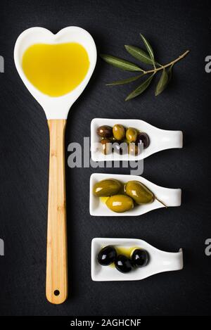 Louche en forme d'un cœur plein d'huile et certains types d'olives sur le fond sombre Banque D'Images