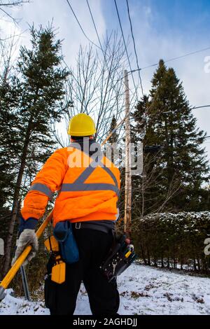 Une fibre optique est ingénieur en vue de l'arrière, travaillant sous un poteau télégraphique à l'extérieur en hiver, le port d'un gilet haute visibilité et casque de sécurité Banque D'Images