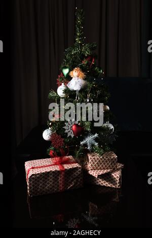 Beau petit et décoré l'arbre de Noël et beaucoup de cadeaux à la maison avec un fond sombre Banque D'Images