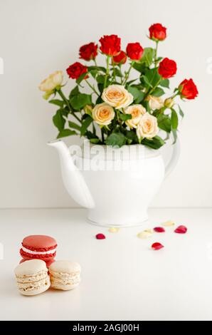 Bouquet de roses de couleur fraîche dans un verre, des pétales et des macarons sur fond blanc. Copier la sace Banque D'Images