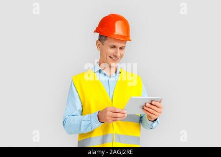 La construction. Man in hardhat et uniforme l'article isolé sur blanc regardant la vidéo sur tablette numérique joyeux sourire Banque D'Images