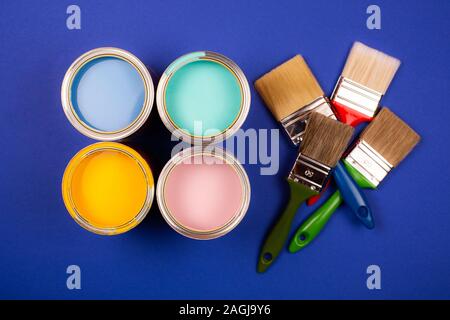 Quatre pots de peinture avec des pinceaux sur fond bleu. Jaune, bleu, rose, turquoise couleurs de peinture. Vue d'en haut. Banque D'Images