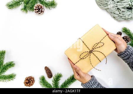 Composition d'hiver de Noël. Main femme boîte cadeau de Noël avec des pommes de pin, branches de sapin sur fond blanc. Mise à plat, vue du dessus, copy space Banque D'Images