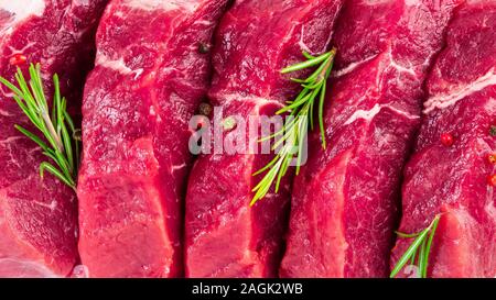 Fond de boeuf en tranches des steaks, l'ail, le romarin et les assaisonnements. Viande juteuse, vue de dessus de la bannière, macro close up. Banque D'Images