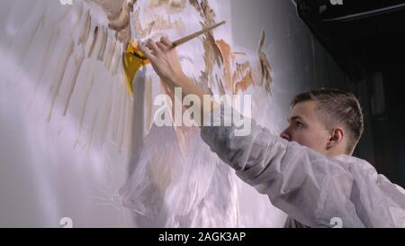 Concepteur de l'artiste dessine un aigle sur le mur. Décorateur artisan photo peintures à l'acrylique couleur d'huile. Peintre peintre vêtu de couche de peinture. À l'intérieur. Banque D'Images