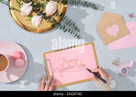 Lettre d'amour Saint Valentin, avec le bloc-notes de concept roses rose, rose macaron, carte sur fond clair. Les mains de fille avec un crayon écrit lettre, qui souhaitent Banque D'Images