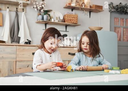 Juste avoir du temps libre. Deux enfants jouant avec des jouets de couleur jaune et orange dans la cuisine blanche Banque D'Images