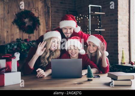 Photo de Papa maman et deux enfants faire x-mas veille vidéo conférence réunion skype en agitant les bras à l'intérieur de la table de séance parents féliciter porter du rouge Banque D'Images