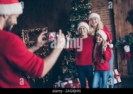 Photo de papa faire photo de frère sœur et maman montrant v-sign près de l'arbre à l'intérieur décoré nouvel an x-mas santa usure spiritueux bouchons et red Banque D'Images