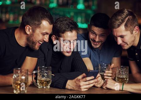 Contenu drôle sur smartphone. Trois amis se reposant dans la pub avec une bière dans les mains. Avoir conversation Banque D'Images