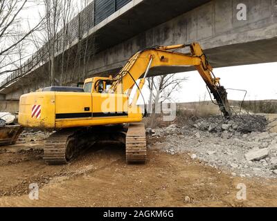 Une exécution d'une pelle de démolition de béton armé avec un marteau hydraulique sous un pont en construction vue depuis l'arrière. Construction site Banque D'Images