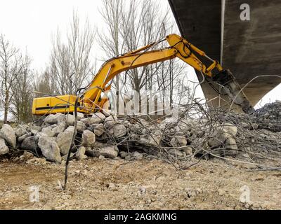 Vue latérale d'une excavatrice l'exécution d'une démolition de béton armé avec un marteau hydraulique sous un pont en construction. Construction site Banque D'Images