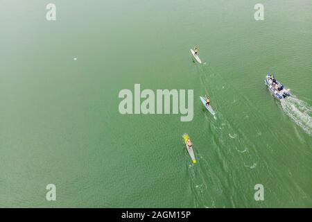 Des hommes forts flottent sur un panneau SUP dans une belle baie par une journée ensoleillée. Vue aérienne des hommes traverse la baie à l'aide du paddleboard. Sports nautiques Banque D'Images