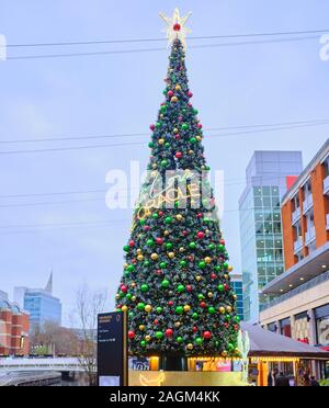 Un grand arbre de Noël qui a été décorée avec de grandes baubles de différentes couleurs et une étoile au-dessus, dans le centre commercial Oracle à Reading, UK Banque D'Images