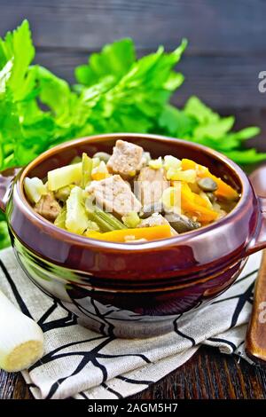 Eintopf soupe de porc, le céleri, les haricots, les carottes et les pommes de terre avec le poireau dans une cuvette d'argile sur planche en bois foncé Banque D'Images