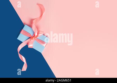 Carte de souhaits avec une boîte-cadeau classique sur fond bleu. Arcs rose. Le centre de la composition. Mise à plat, vue du dessus. Banque D'Images
