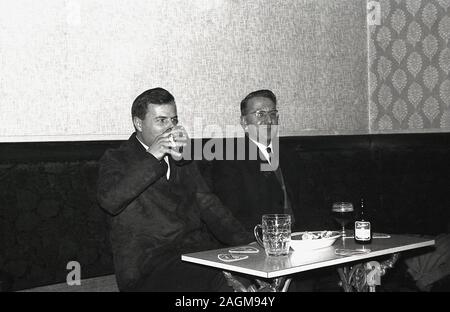 Années 1960, historiques, deux hommes bien habillés assis dans un coin d'un bar ou pub, boire de la bière, avec l'un d'entre eux ayant une bouteille de Dutton's Pale Ale, England, UK. Banque D'Images