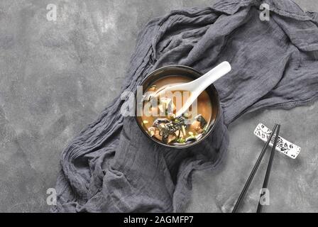 Soupe japonaise miso avec thon frais, algues séchées, tofu, champignons shiitake séchés dans un bol noir sur fond gris Banque D'Images