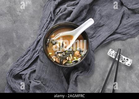 Soupe japonaise miso avec thon frais, algues séchées, tofu, champignons shiitake séchés dans un bol noir sur fond gris Banque D'Images