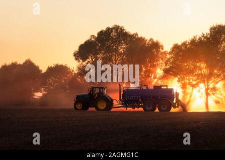 La pulvérisation d'engrais du tracteur sur terrain au coucher du soleil, les nuances de couleurs luxuriantes de lave, près de Schwabisch Hall, en Allemagne. Agriculteur avec un tracteur sur un champ agricole. Banque D'Images