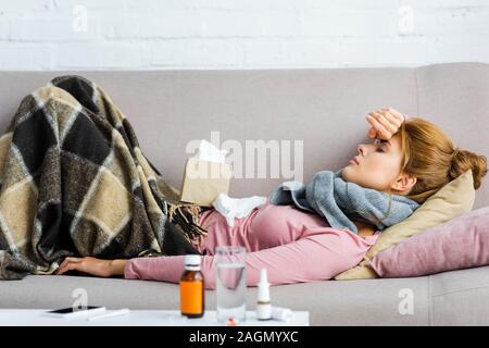 Vue latérale d'attrayants et femme malade en gris foulard avec maux de tête couché dans l'appartement Banque D'Images