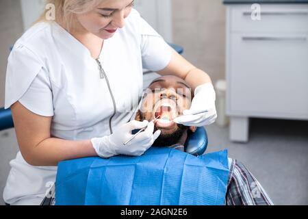 Les jeunes africains-américains en visite de l'homme Bureau du dentiste dans la prévention et le traitement de la cavité orale. L'homme et la femme médecin tout checkup des dents. Vie saine, santé et médecine concept. Banque D'Images