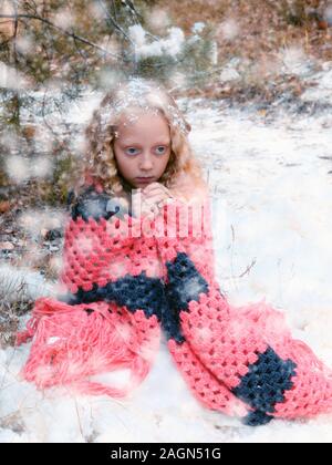 Peu triste fille congelé dans la forêt d'hiver. jeune fille dans la forêt d'hiver, assis, enveloppé dans une écharpe, essayant de garder au chaud Banque D'Images